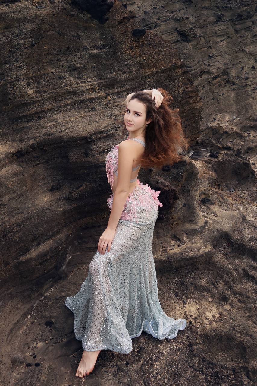 Angelina seated on a rock looking over her shoulder in a sequined gown