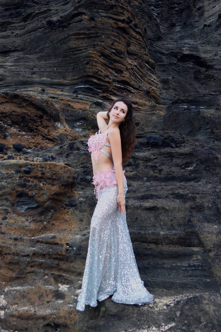 Angelina against a rock wall in a silver mermaid-tail gown